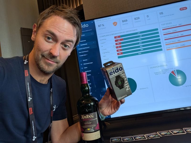 A member of the Eido team holding a bottle of whisky beside a screen showing an Eido dashboard.