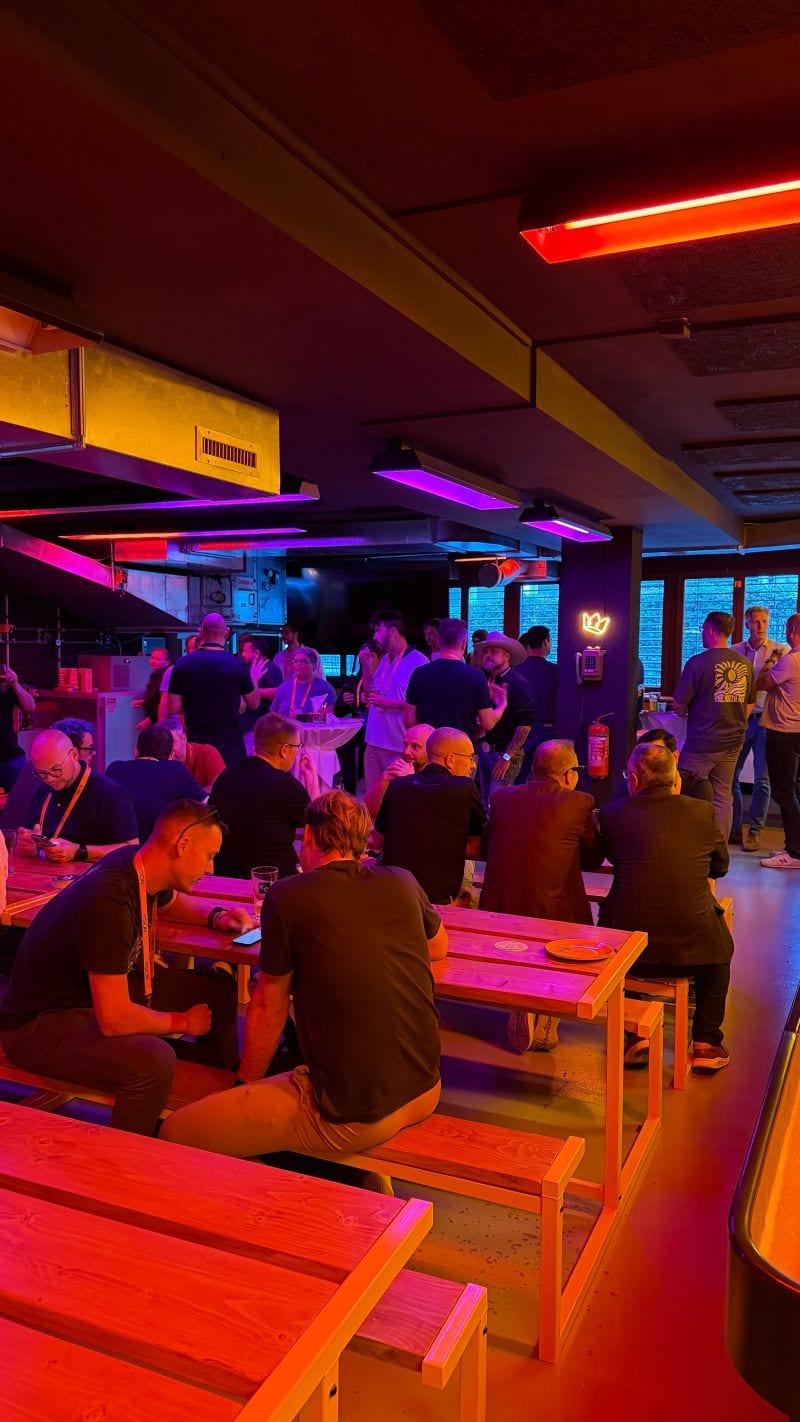 The venue during the evening, with groups of people at long tables under neon light.